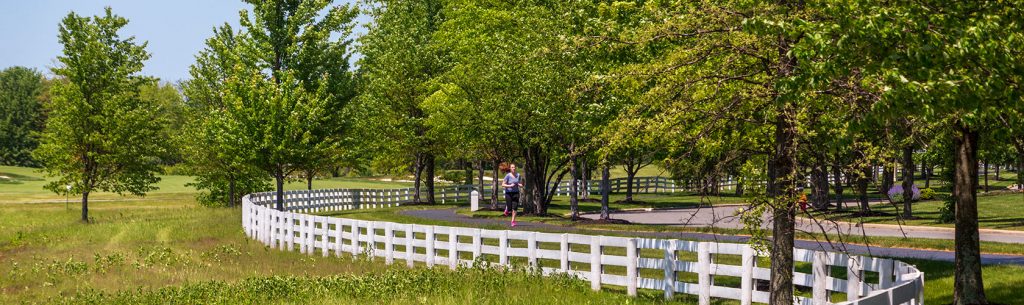 Runner on path with curved white fencing under a blue, sunny sky in summer.