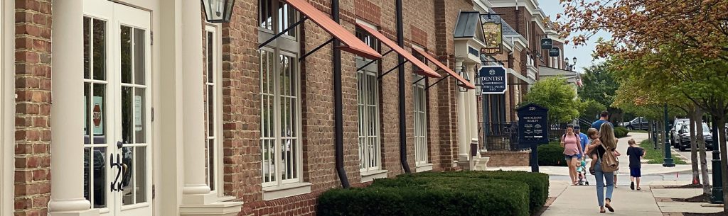 People walking down sidewalk on Market Street past red brick office building in New Albany, Ohio